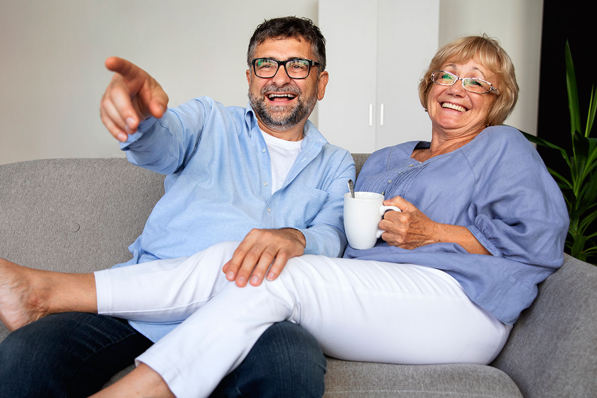 people watching tv and laughing mature couple at home
